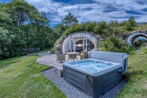 A hot tub with a stone wall backdrop, outdoor seating area, and a view of a natural landscape. - The Warren - Hobbit House & Hot Tub at Loch Tay (Perth and Kinross)