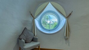 A room with a stone floor, a round window with curtains, and a grey chair.