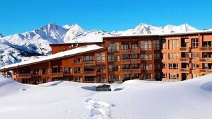 Ein mehrstöckiges Hotel mit Holzfassade, großen Fenstern und Balkonen vor einer Kulisse schneebedeckter Berge.