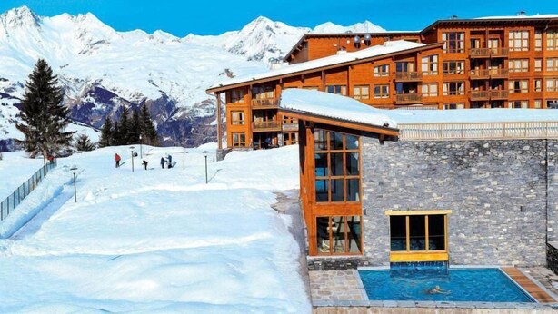 Ein schneebedecktes Bergresort mit Poolbereich und Holzhäusern.