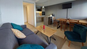 Un salon moderne avec un canapé gris, des coussins turquoise et à motifs, une table basse en bois et un coin repas avec un téléviseur fixé au mur.