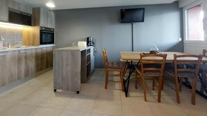 Une cuisine moderne avec un coin repas, un téléviseur à écran plat fixé au mur et une fenêtre laissant entrer la lumière naturelle.