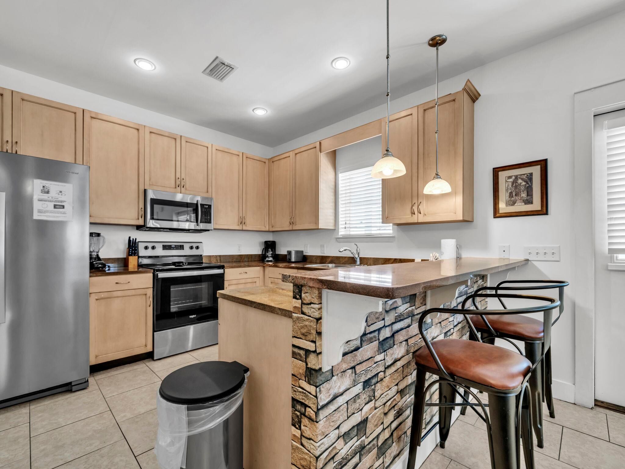 A modern kitchen with wooden cabinets, stainless steel appliances, a granite countertop, and a stone backsplash.