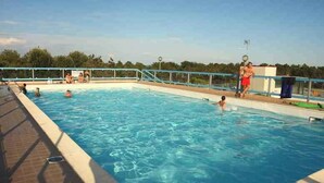 A swimming pool with clear blue water, surrounded by a tiled deck and a metal railing. - Holiday apartment mit Balkon (Bibione)