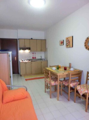 Un espace de vie compact comprenant un coin cuisine, un coin repas avec une table et des chaises, et un lit simple.