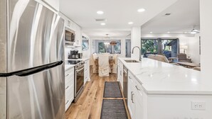 A modern kitchen with stainless steel appliances, a large island, and a dining area with a view. - Peaceful Villa Just Steps to Beach in Sea Pines (Hilton Head Island)