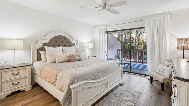A bedroom with a large bed, a ceiling fan, a nightstand, a chair, and a view of the outdoors. - Peaceful Villa Just Steps to Beach in Sea Pines (Hilton Head Island)