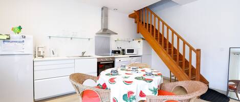 Une cuisine avec des meubles blancs, un four à micro-ondes, une cuisinière et une table à manger entourée de chaises en osier.