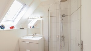 Ein modernes Badezimmer mit Oberlicht, einer Dusche und einem Waschtisch mit Spiegel.