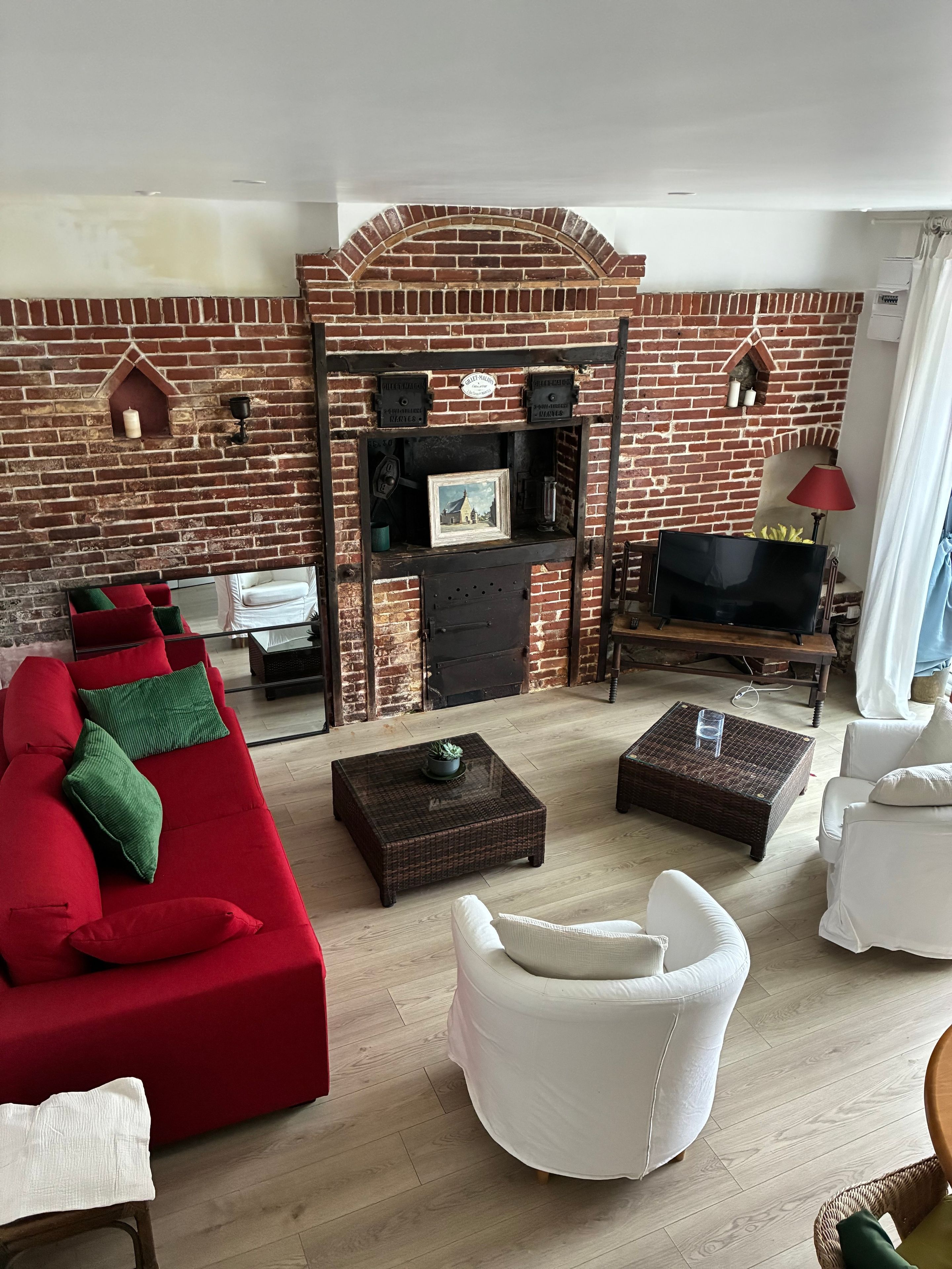 Una sala de estar con chimenea de ladrillo, sofás blancos y rojos, un televisor y una lámpara roja.