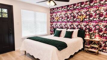 A bedroom with a bed, a ceiling fan, a window with blinds, and a floral wallpaper.