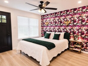 A bedroom with a bed, a ceiling fan, a window with blinds, and a floral wallpaper.