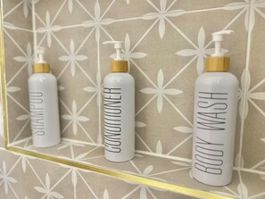 Three bottles of shampoo, conditioner, and body wash on a bathroom shelf.