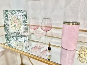 A glass table with pink wine glasses, a pink tumbler, and a decorative mirror with floral patterns.