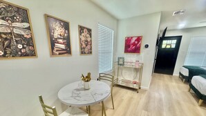 A dining area with a round table, two chairs, and a gold-framed glass cabinet with decorative items. - Welcome to The Pink Peony on Market Street in historic downtown Brenham. (Brenham)