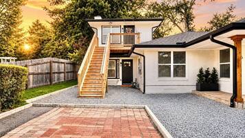 A two-story house with a wooden staircase leading to the upper level, a covered porch, and a gravel driveway.