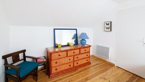 Una stanza con pavimento in legno, una panca di legno con cuscino, una cassettiera in vimini, uno specchio e una lampada.