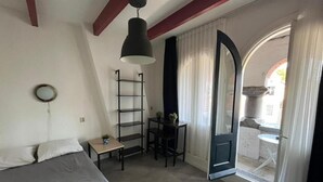 A bedroom with a bed, a desk, a chair, a shelf, and a door leading to an outdoor area.