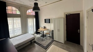 A bedroom with a bed, a desk, a chair, a TV, and a wardrobe.