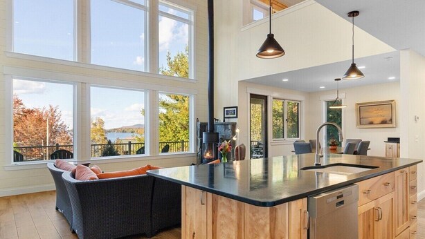 A spacious kitchen with large windows, a central island, and a dining area with a sofa. - Modern Dreamy Moosehead Home - Lake Views, Walk to (Greenville)