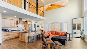 A spacious open-plan living area with a kitchen, a dining area, and a seating area with a sofa and chairs. - Modern Dreamy Moosehead Home - Lake Views, Walk to (Greenville)