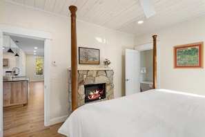 Un dormitorio con chimenea de piedra, una cama y vistas a la cocina y el baño.