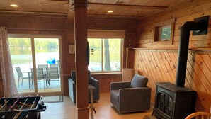 L’intérieur chaleureux d’un chalet avec un poêle à bois, une table de baby-foot et un coin repas comprenant une table et des chaises.