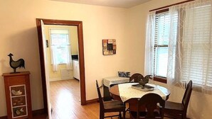 A dining area with a wooden table and chairs, a wooden cabinet with decorative items, a bulletin board, and a window with curtains. - Charming 2-bedroom house in fabulous downtown Hermann (Hermann)