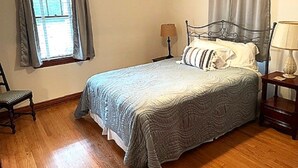 A bedroom with a bed, a chair, a nightstand, a lamp, and a window with curtains. - Charming 2-bedroom house in fabulous downtown Hermann (Hermann)