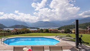 Une piscine avec une terrasse en bois, des chaises longues et une vue sur les montagnes et un lac.