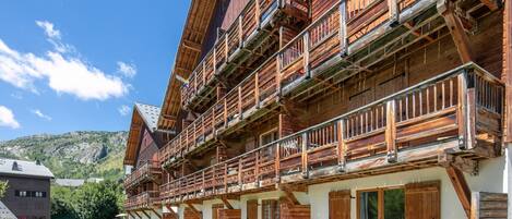 A multi-story wooden building with balconies, a grassy courtyard, and a mountain backdrop.