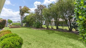 A well-maintained lawn with various trees and shrubs, a wooden bench, and a clear sky.