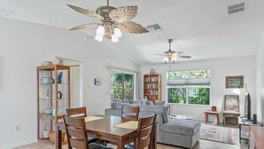 A spacious living area with a dining table, sofas, and a ceiling fan.