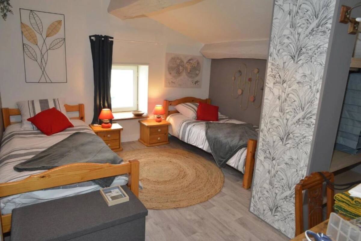 Une chambre confortable avec deux lits, une tête de lit en bois, une table de chevet avec une lampe, un tapis tissé et un mur orné d’un motif de feuilles.