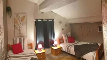 Une chambre double avec deux lits, chacun doté de draps à rayures et d’oreillers rouges. On y trouve des tables de chevet avec des lampes, un téléviseur fixé au mur et un plafond avec des poutres apparentes.