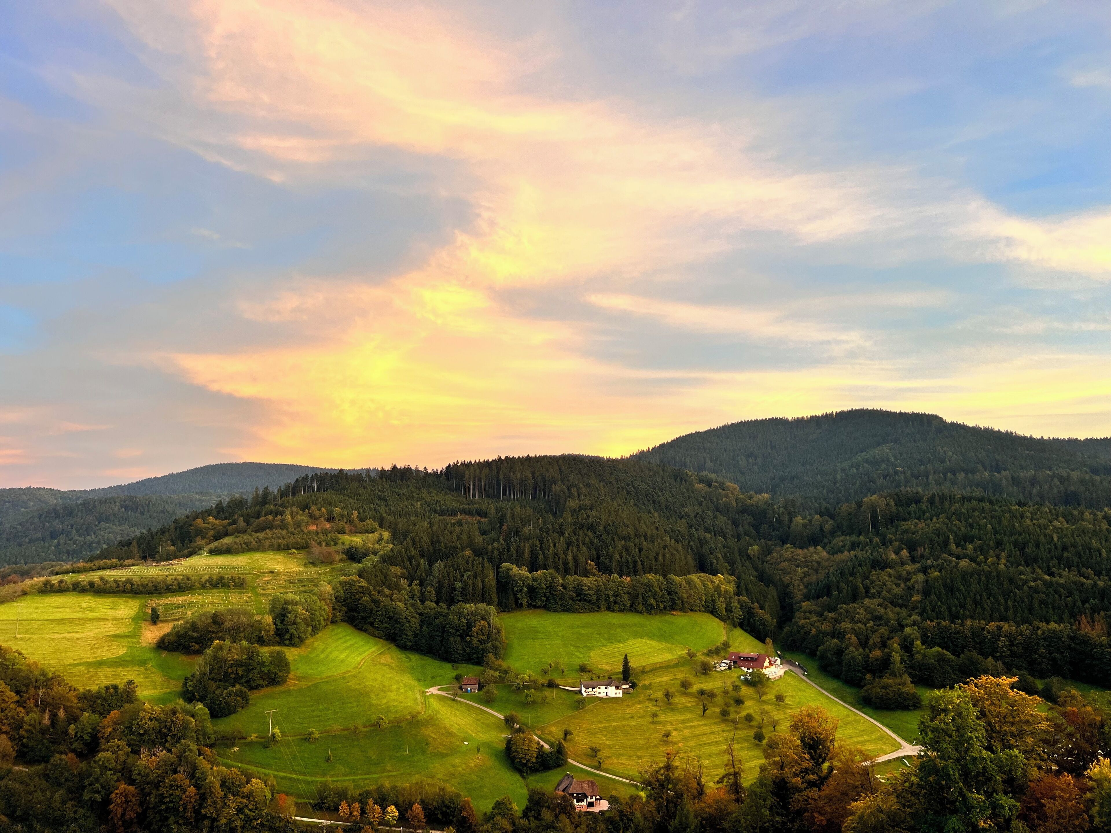 A rural landscape with rolling hills, a small cluster of houses, and a winding road.