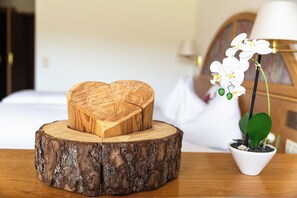A wooden heart-shaped box on a tree stump, a potted orchid, and a bed with white linens in the background.