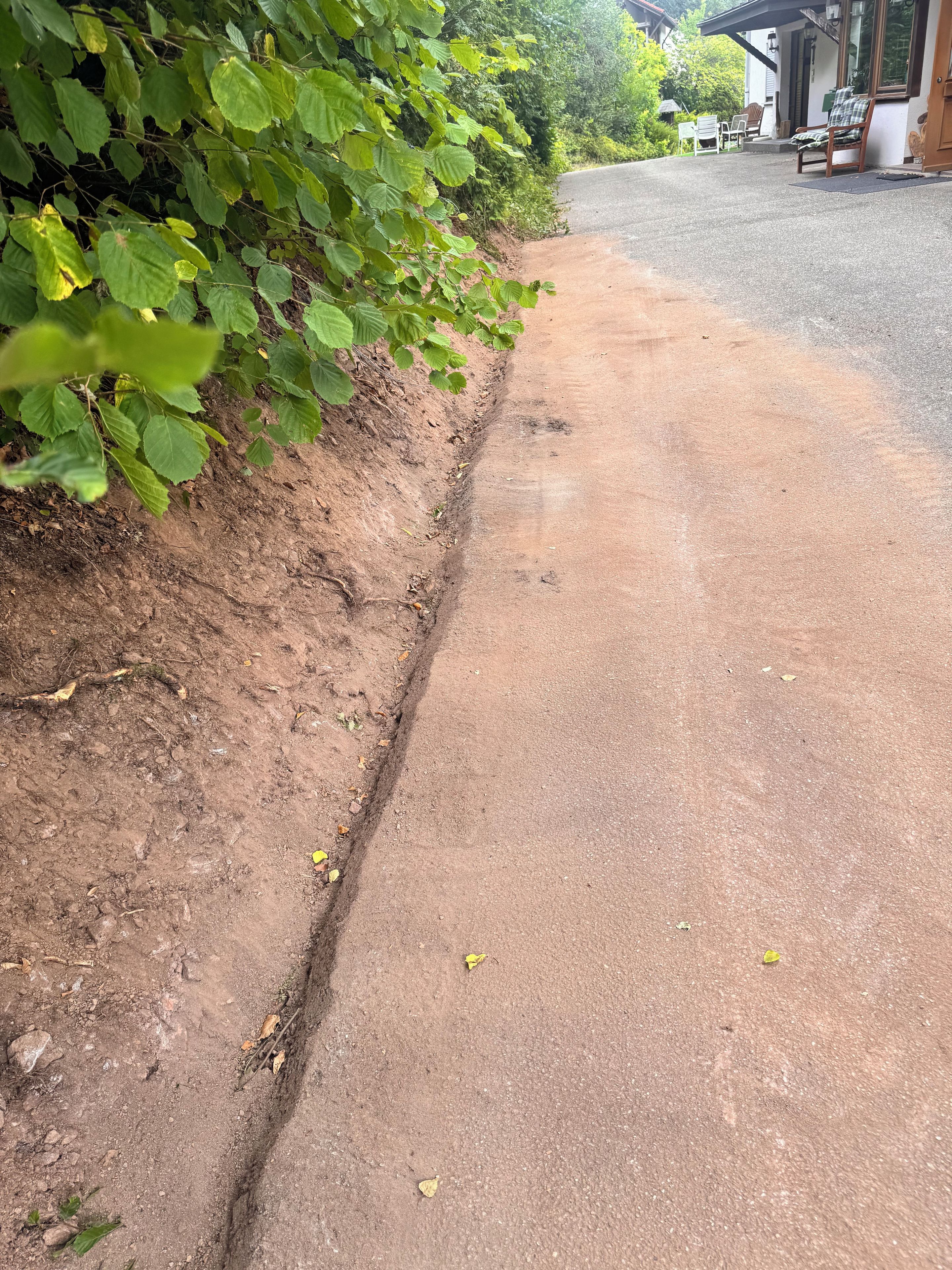 A paved pathway adjacent to a building with a dirt embankment on one side.