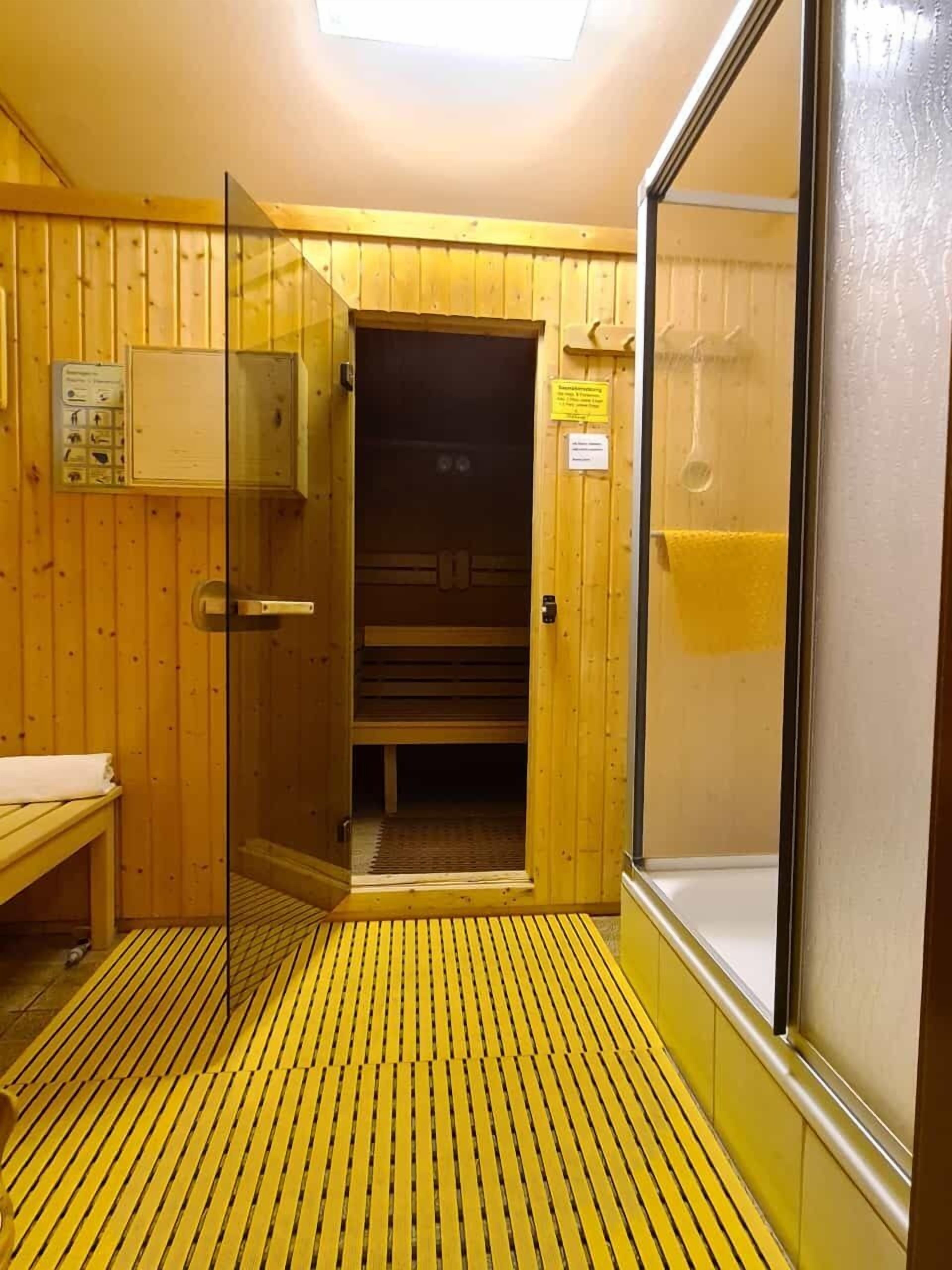 A sauna room with wooden walls, a bench, a glass door, and a control panel.