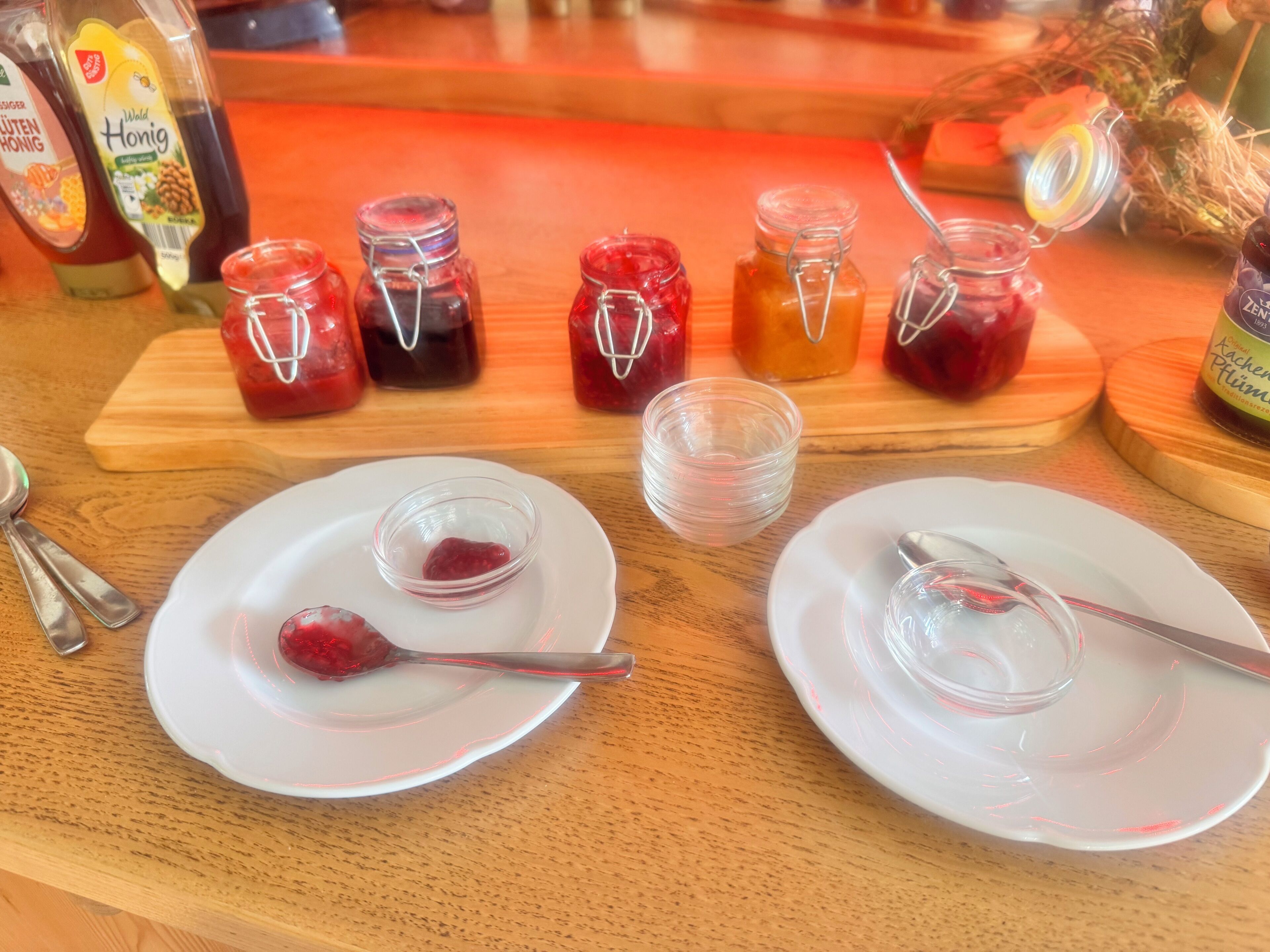A table with several glass jars containing different types of preserves, accompanied by white plates and spoons.