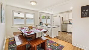 A modern kitchen with white cabinetry, a wooden dining table, and a colorful rug. - Cozy Pet & Family-friendly fully fenced beautiful  backyard (Arvada)