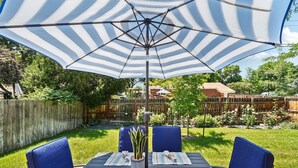 A patio with a table, blue chairs, striped tablecloths, and a large striped umbrella. - Cozy Pet & Family-friendly fully fenced beautiful  backyard (Arvada)