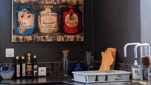 Een keuken met een modern design, voorzien van een donkere spatwand, een RVS spoelbak en diverse flessen op het aanrecht.