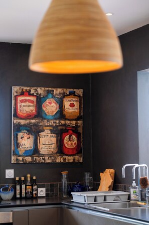 Een keuken met een modern design, voorzien van een donkere spatwand, een RVS spoelbak en diverse flessen op het aanrecht.