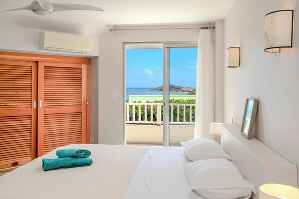 Habitación de hotel con cama, armario de madera, balcón con vista al mar y ventilador de techo.