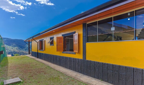 Un bâtiment jaune, doté de volets en bois et de grandes fenêtres, se dressant sur un fond de paysage montagneux.