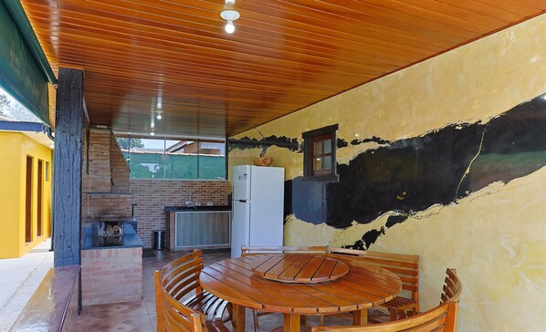 Una mesa de comedor de madera con sillas, una chimenea de ladrillo y un refrigerador blanco en una habitación con pared amarilla y techo de madera.