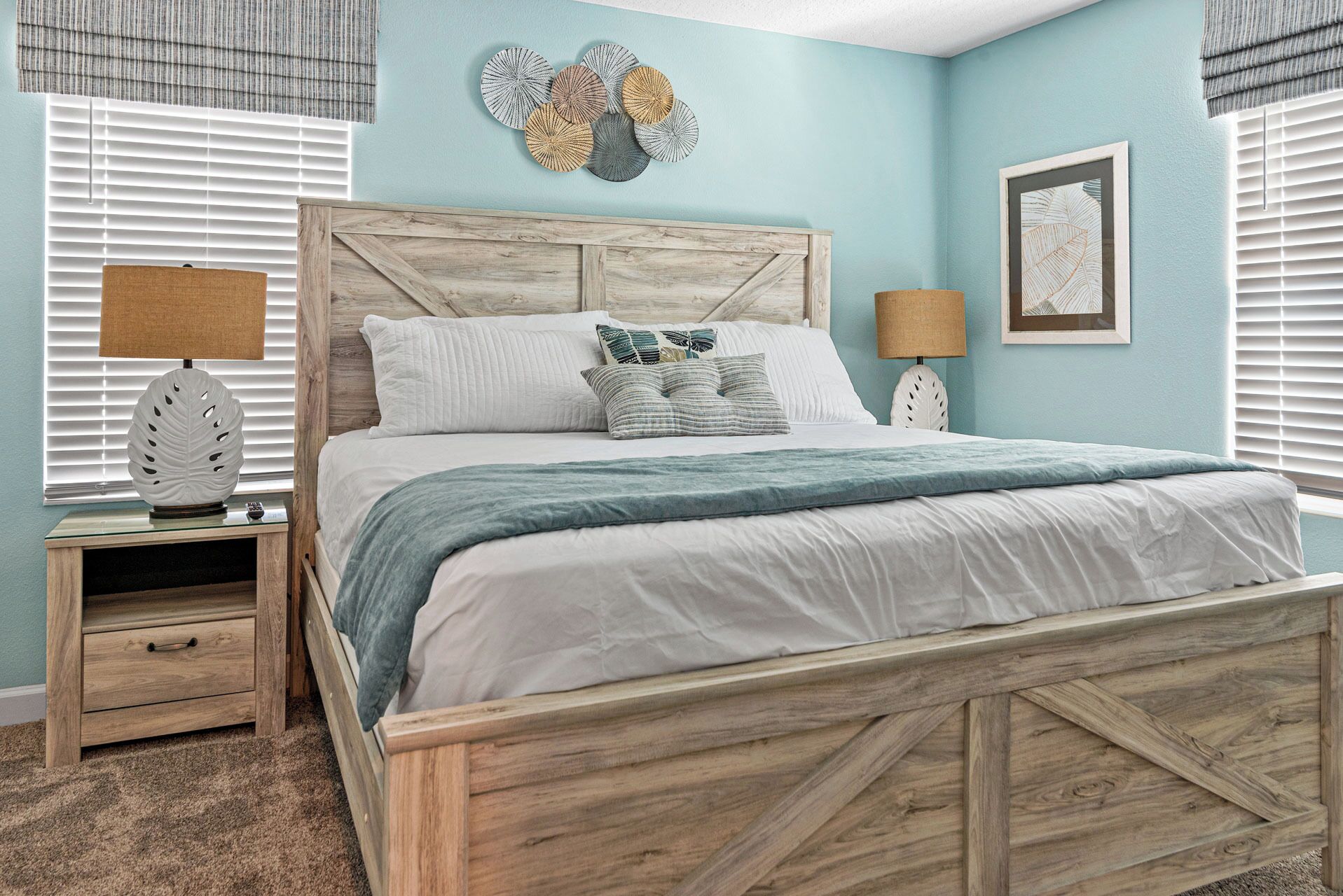 A bedroom with a wooden bed frame, a bedside table with a lamp, and a wall art piece above the bed.