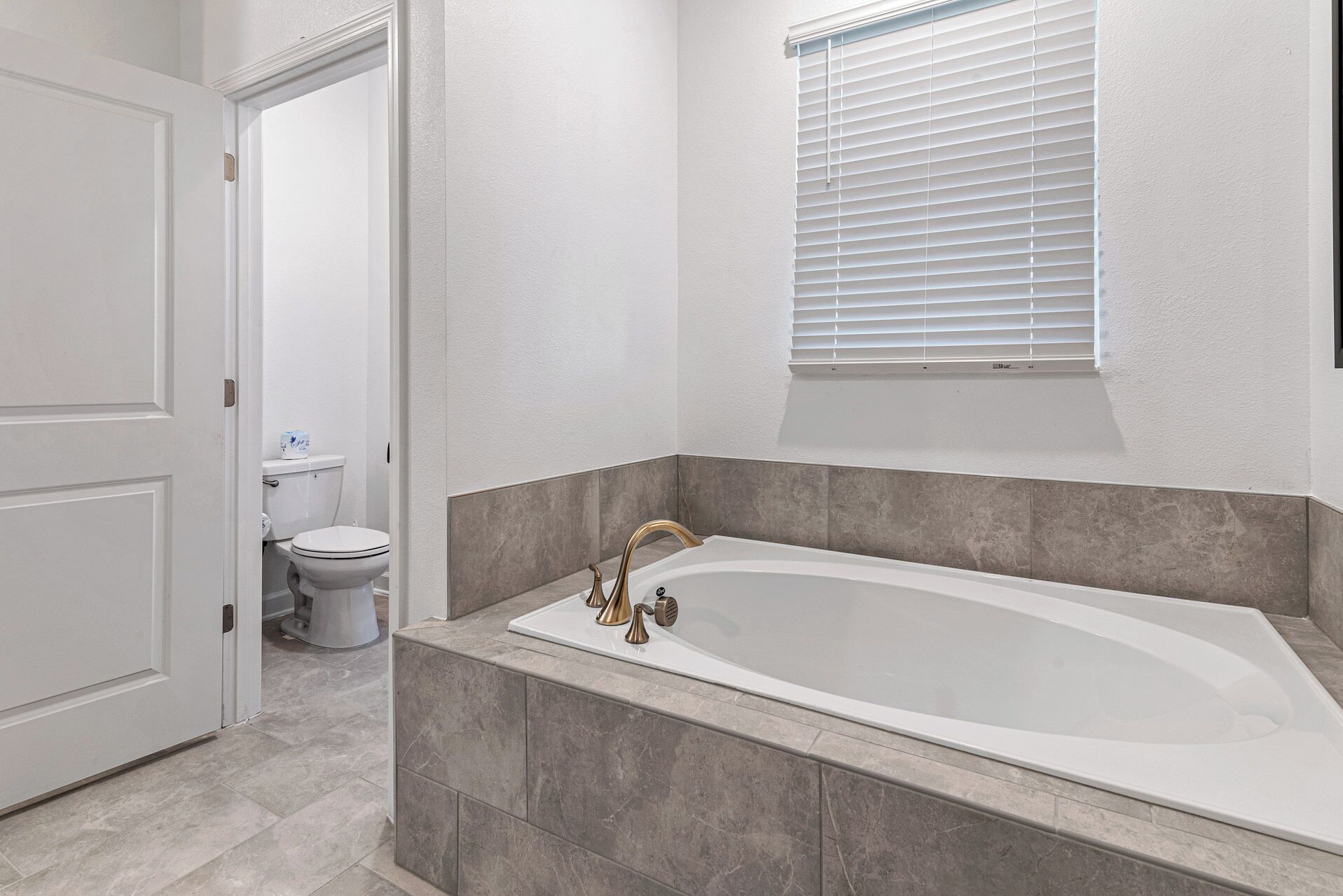 A bathroom with a bathtub, toilet, and window.