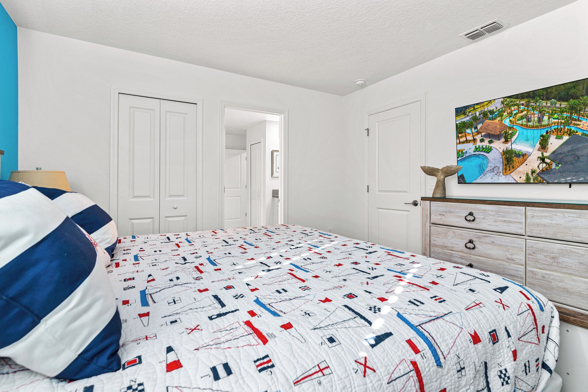 A bedroom with a bed, a dresser, and a painting of a resort.